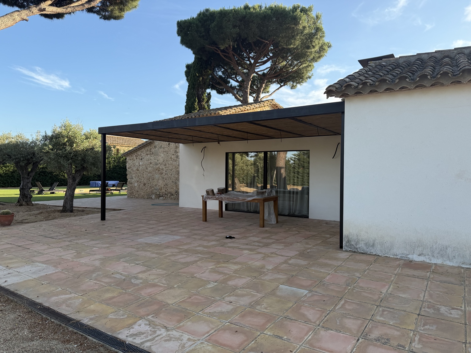 Pérgola metálica con cubierta de cañizo junto a una vivienda